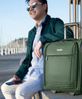 Man seated outdoors with Underseat Carry-On Luggage With 28L Capacity, Sustainable Travel Bag Made From Recycled RPET in Juniper Green next to him