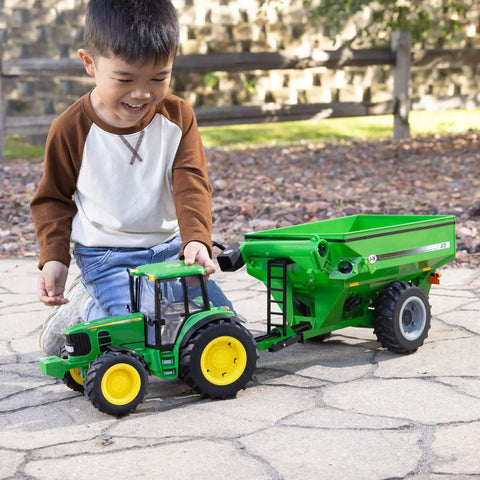 Child playing with One Sixteenth Scale Big Farm 7430 Tractor With Grain Cart Toy Set Featuring Lights And Sounds For Kids outdoors.