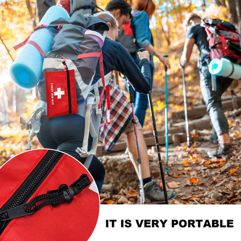 Red first aid kit pouch with zipper and white cross; clipped to a hiking backpack outdoors.