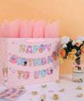 13 Inch Large Cat Birthday Gift Bag Set With Handles, Greeting Card, Pink Tissue Paper, Kitty Themed Stickers, Banner next to flowers
