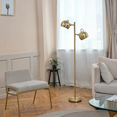 Miles 61 Inch Two Light Floor Lamp in Matte Brass Finish with Adjustable Heads and In Line On Off Foot Switch Mid Century Modern Style Tall Space Saving Accent Lamp for Living Room or Bedroom standing beside a chair in a modern living room.
