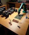 Workbench setup with RC vehicle, robotic arm, and circuit board, showcasing Two Pack Four Channel RC Transmitter And Receiver Set For 27MHz Remote Control Boards Built For Robot Models Drones And DIY Smart Vehicles With Easy Multi Channel Control And Rock Solid Performance.