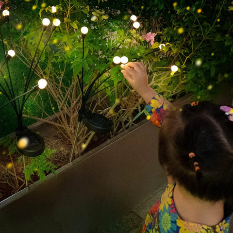 Child interacting with 8 Pack 64 LED Solar Firefly Garden Lights Waterproof Outdoor Swaying Fairy Lights For Patio Yard Pathway Romantic Wind Driven Decor Easy Setup Energy Saving Landscape Lighting glowing among garden greenery.