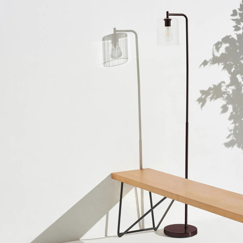 Tall Edison Bulb Floor Lamp With Glass Shade In Bronze Finish next to wooden bench, casting shadow on white wall, indoor setting