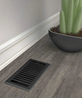 Montezuma 4 By 10 Inch Decorative Floor Register in Black Iron beside plant on wooden floor