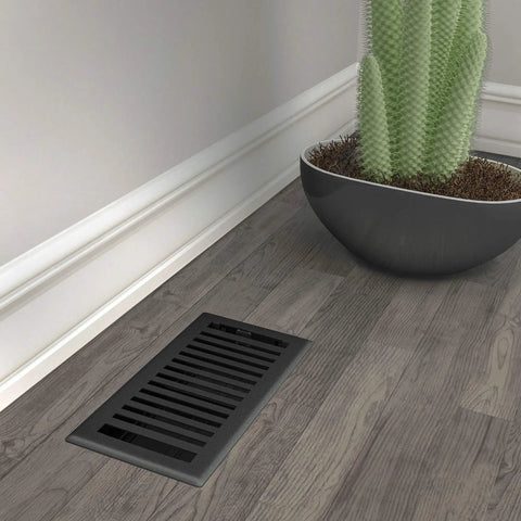 Montezuma 4 By 10 Inch Decorative Floor Register in Black Iron beside plant on wooden floor
