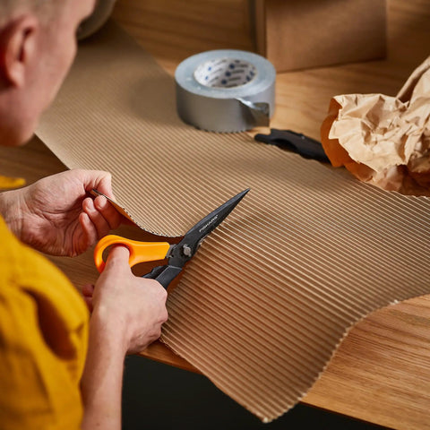 Person using All In One Garden Tool 7-In-1 Pruning Shears For Plant Care With Titanium Knife, cutting cardboard on a table.