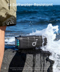 Compact outdoor speaker with floating playback stays upright in waves IP68 waterproof saltwater resistant on rocky shore.