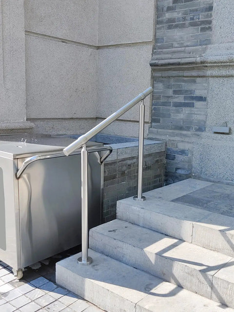 Hella Sturdy 3 Step Outdoor Handrail With Zero Sweat Diy Install Pack And Rugged 304 Stainless Steel Build For Porch Stairs On Concrete Brick Or Wood Planks Silver Finish Smooth Ride installed on concrete stairs next to a metal cart.