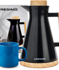 Vacuum Insulated Thermal Carafe 34 Oz Keeps Coffee Hot for 12 Hours with Glass Wall and Beech Wood Accents next to blue mug