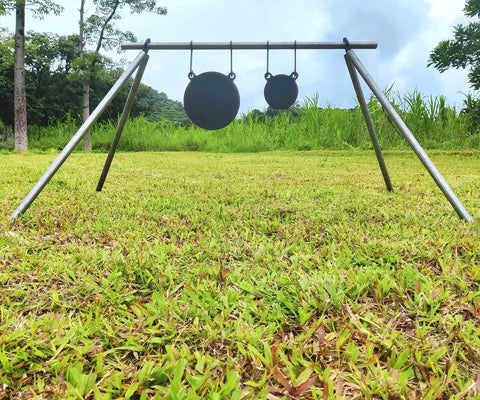 Range setup with AR500 Steel Gong Target 3 Eighths Inch Thick For Precision Shooting, mounted on a tripod in a grassy field.