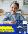 Child holding glass with Hard Water Test Strips Kit with Dual Color Pads, 150 strips and sample tube on table.