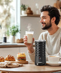Man enjoying coffee next to 4 In 1 Electric Milk Frother For Hot And Cold Foam, Temperature Control And Auto Shut Off, on kitchen counter.