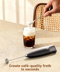 Handheld Milk Frother Wand With 2 Whisks, Electric Coffee Mixer for creamy foam, placed on a table next to iced coffee.