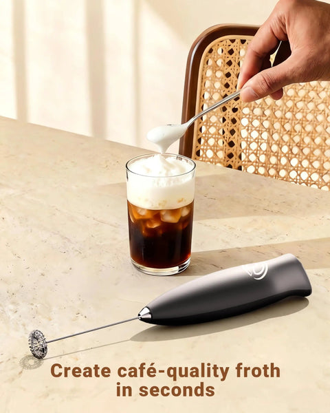 Handheld Milk Frother Wand With 2 Whisks, Electric Coffee Mixer for creamy foam, placed on a table next to iced coffee.