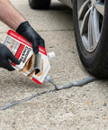 Using Two Pack 2.2 Pound Grey Concrete Crack Filler Self Leveling Sealant For Driveways on cracked pavement near car tire.