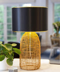 Black drum lampshade, 13 inch diameter, modern design with spider fitter, atop a woven base on a table, cozy ambience lighting.