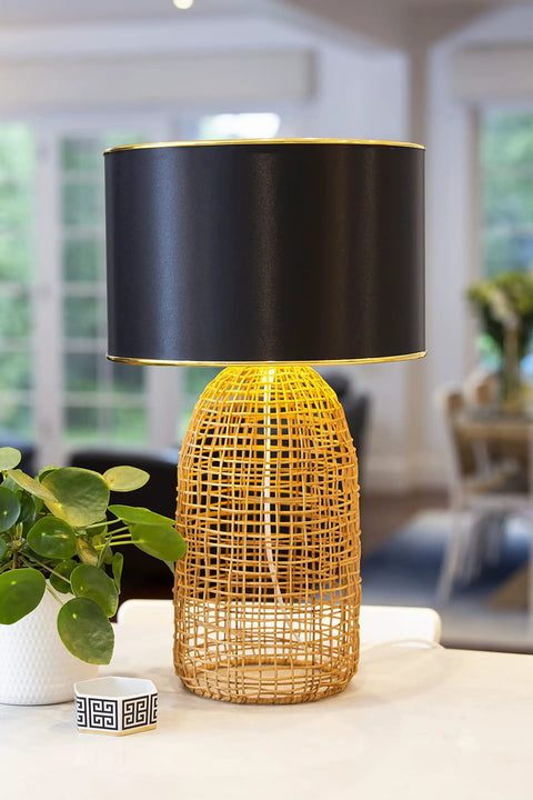 Black drum lampshade, 13 inch diameter, modern design with spider fitter, atop a woven base on a table, cozy ambience lighting.