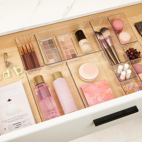 Level Up Your Vanity Game With This 10 Piece Clear Drawer Organizer Set arranged in a tidy vanity drawer with cosmetics and brushes.