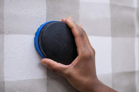Hand using wallpaper scoring tool with four steel blades, no slip grip, strips and removes wallpaper fast on wall surface.