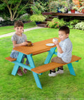 Two children sitting at Wooden Outdoor Kids Picnic Table And Bench Set In Brown And Aqua, on lawn, enjoying snacks.