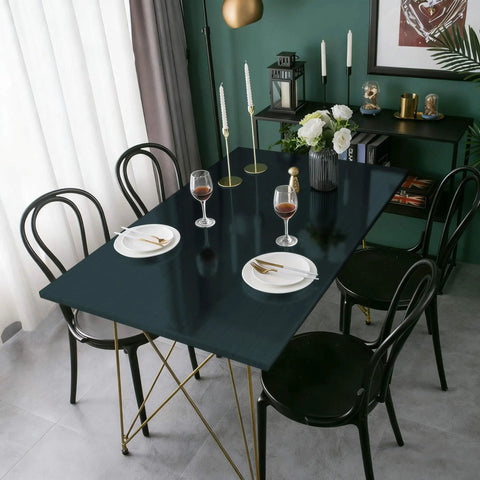 Dining table setting with dark green waterproof metallic wallpaper countertop on gold legs surrounded by black chairs.
