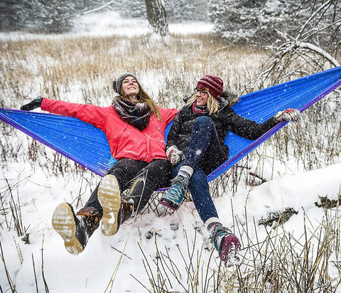 Two people sitting in a DoubleNest Lightweight Camping Hammock For 1 To 2 People With 400 Lb Capacity, 9.5 Ft Long, Royal Navy Color in snow.