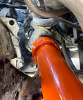 Orange inner tie rod removal tool installed on a vehicle's steering rack area (undercarriage view).