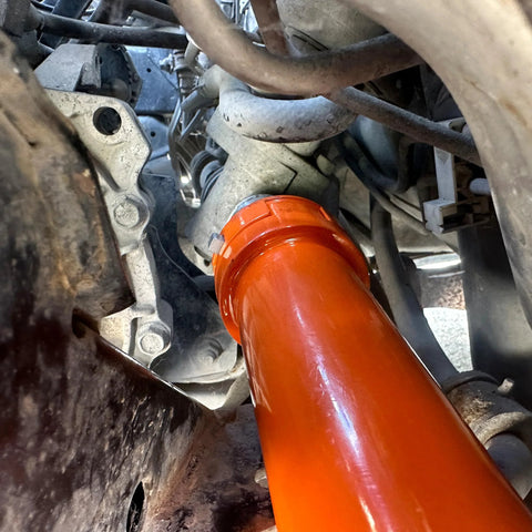 Orange inner tie rod removal tool installed on a vehicle's steering rack area (undercarriage view).