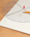 Front view of a 10-inch round clear acrylic center finder compass with black concentric circle marks, pencil nearby.