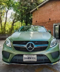 Front view of a Mercedes car with Quebec plate, parked outdoors by a brick building and trees in background