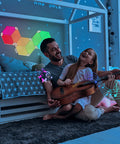 Father and daughter playing guitar in room lit by Rhythm Edition Smart Triangle RGB LED Wall Light Panels 9 Pack Dope Mood Lighting.