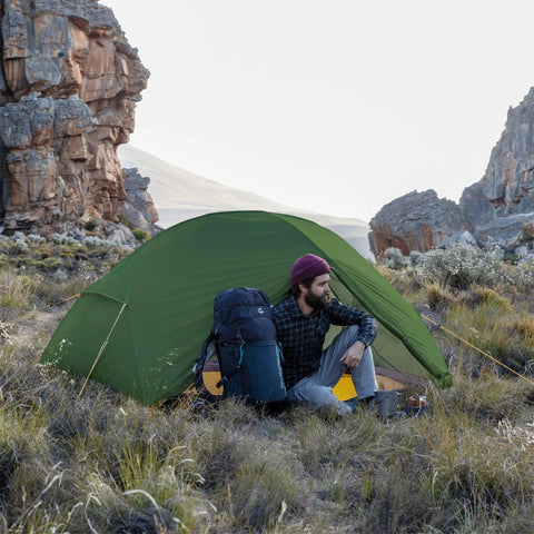 Man sitting by Mongar 2 Person Backpacking Tent for 3 season camping in a rocky landscape.