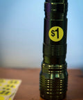 Metal flashlight with a $1 neon sticker from Yard Sale EZ Kit Neon Yellow Signs 11 By 14 Inches With 600 Prepriced Stickers. Wooden background.