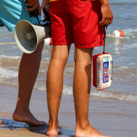 Two people on the beach, one holding Marine Waterproof First Aid Kit For Boat Kayak And Beach With Floating Hard Case And Emergency Medical Supplies.