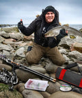 Man holding fish beside Carbon Fiber Telescopic Fishing Rod Kit With Spinning Reel, Line, Lures, Hooks And Carrier Bag For Newbies, Saltwater And Freshwater Angling, 2.1M All In One Gear Set on rocks by the sea.