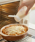 Top Shelf Soft Parmesan Cheese Shaker Set Squeezable Spice Jars With Wide Opening Heavy Duty Plastic Seasoning Dispensers being used to sprinkle cheese over a dish.