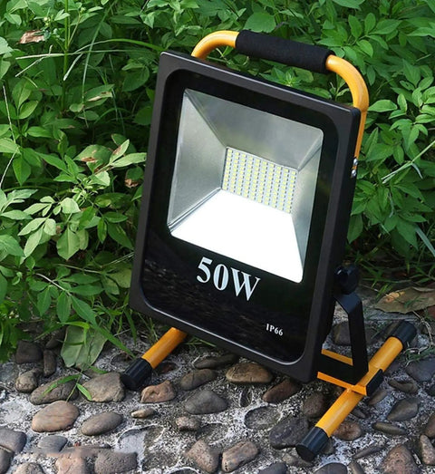 Spot Lighting 50W Led Rechargeable Construction Floodlight, 5000Lm Sup, with sturdy stand on rocky ground surrounded by green foliage.