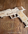 Wolf 01 Handgun 3D Puzzle Rubber Band Gun Mechanical Model Kit For DIY Wood Build, Collectible Hobby Craft, Brain Teaser Puzzle With 60 Rubber Bands, Fires Up To 5 Per Round, 10 Meter Range, Secret Handle Compartment, Torch Mount. Wooden rubber band handgun kit with bands on wood surface.