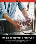Person filling a clear 70-oz removable reservoir of Programmable XL 14 Cup Barista Grade Coffee Maker Pro at a sink.