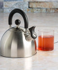 Whistling Stovetop Tea Kettle With Food Grade Stainless Steel, 1.5 Quart Capacity, Brushed Finish With Black Handle next to tea mug