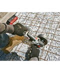 Professional 20V Max 4.5 Inch Angle Grinder cutting rebar on gravel surface with gloves and work boots.