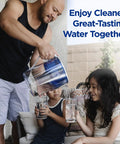 Water pitcher (blue) being poured into two glasses for kids by a man in a home setting.
