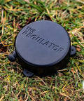 Hidden Self Retracting Cornhole Measuring Device For Regulation 27-Foot Distance Between Boards, No Tangled Rope Or Tape, Quick Setup, Discreet Accessory That Stays Ready During Gameplay. Black round cornhole distance regulator on grass