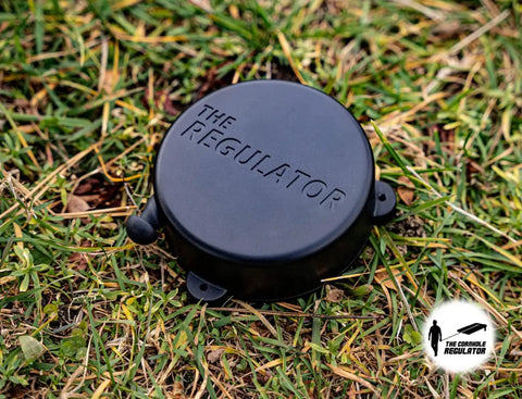 Hidden Self Retracting Cornhole Measuring Device For Regulation 27-Foot Distance Between Boards, No Tangled Rope Or Tape, Quick Setup, Discreet Accessory That Stays Ready During Gameplay. Black round cornhole distance regulator on grass