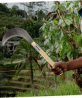 Man holding Long Handle Manganese Steel Grass Sickle For Weeding And Harvesting, Hand Tool With Wooden Grip in lush field
