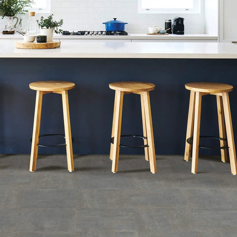 Grey Tundra Peel And Stick Floor Tiles for easy DIY flooring shown under wooden stools in a modern kitchen setting.