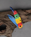 Colorful Parrot Pattern Folding Pocket Knife With Gradient Parrot-Scale Handle, 3-Inch Blue Coated Blade, on wood background