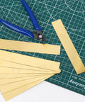 10 Piece Brass Shim Stock Set 6 Inch Long By 1 Inch Wide 0.002 Inch Thick Brass Strips on cutting mat with tool