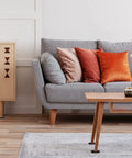 Modern living room with a gray sofa, orange and beige cushions, light wooden coffee table and cabinet, decorated with vases.